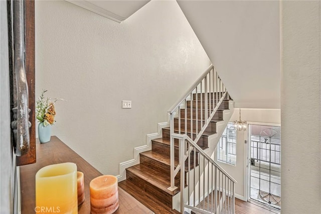 stairs featuring wood finished floors, a chandelier, baseboards, and a textured wall