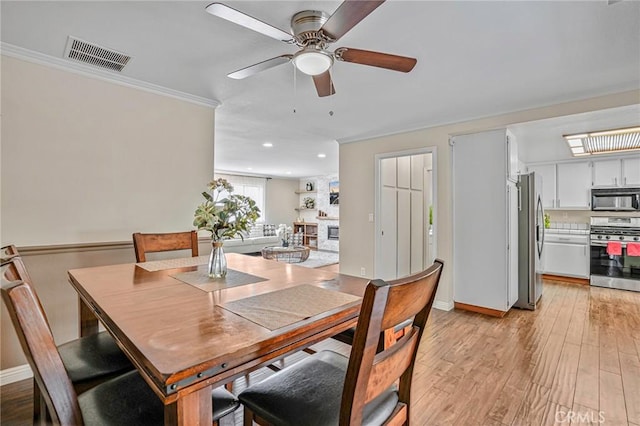 dining room featuring a ceiling fan, crown molding, light wood finished floors, recessed lighting, and a large fireplace