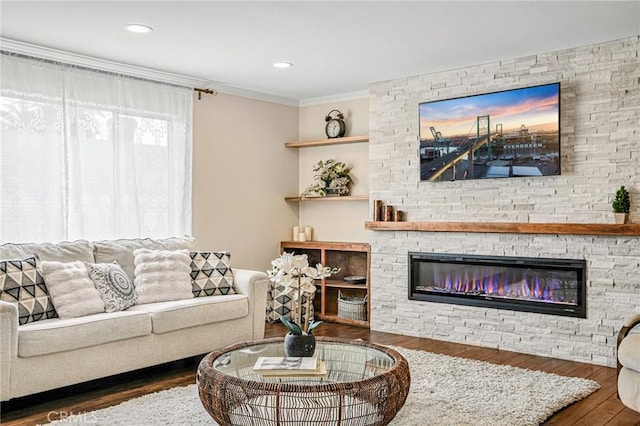 living area with wood finished floors, a stone fireplace, and crown molding