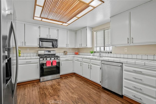 kitchen with appliances with stainless steel finishes, white cabinets, dark wood-type flooring, and tile counters