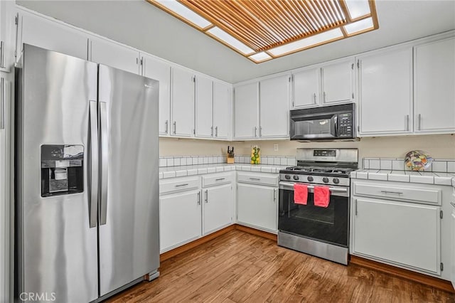kitchen featuring stainless steel appliances, tile counters, wood finished floors, and white cabinetry