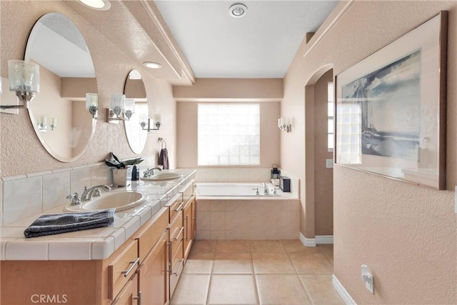 full bath featuring a garden tub, tile patterned flooring, a textured wall, double vanity, and recessed lighting