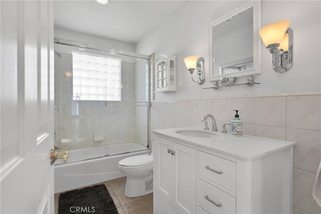 full bathroom with tile patterned floors, tile walls, toilet, vanity, and shower / bath combination with glass door