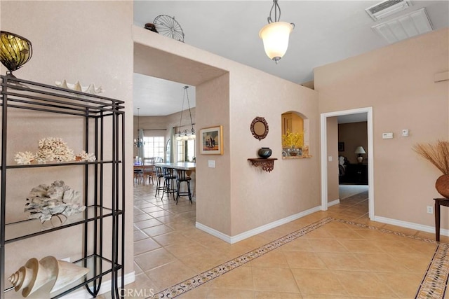 hallway with light tile patterned floors, baseboards, a chandelier, and arched walkways