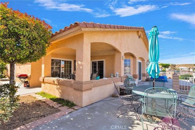 rear view of property with stucco siding, a patio, outdoor dining area, and fence