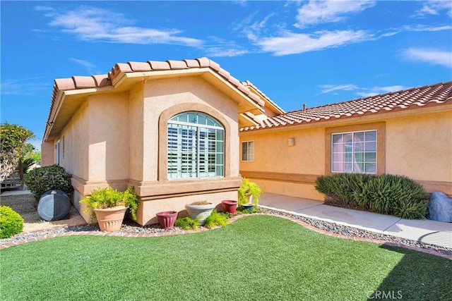 view of side of property with a yard, a tile roof, and stucco siding