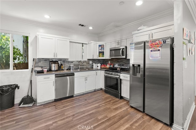 kitchen with appliances with stainless steel finishes, light wood finished floors, white cabinetry, decorative backsplash, and recessed lighting