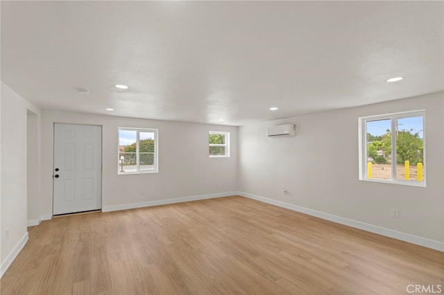 spare room featuring light wood-style flooring, a wall unit AC, recessed lighting, healthy amount of natural light, and baseboards