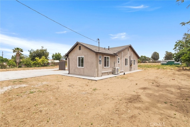rear view of house with stucco siding, central AC unit, and driveway
