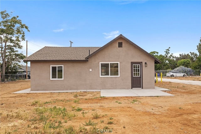 rear view of house featuring fence, stucco siding, a patio area, and a shingled roof