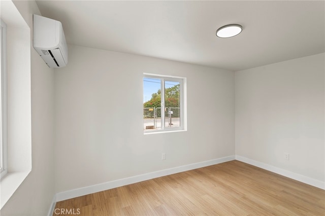 empty room featuring a wall mounted air conditioner, light wood finished floors, and baseboards