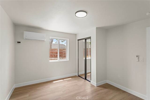 unfurnished bedroom featuring a wall mounted AC, light wood-style flooring, a closet, and baseboards