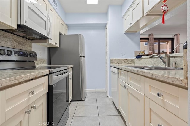 kitchen with white appliances, a sink, light tile patterned floors, light stone countertops, and baseboards