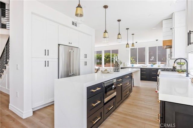 17 Candlewood, Irvine, CA 92620 - kitchen featuring appliances with stainless steel finishes, white cabinetry, light countertops, and light wood-style floors