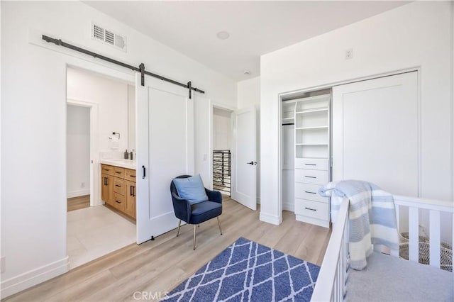 17 Candlewood, Irvine, CA 92620 - bedroom featuring a barn door, light wood-type flooring, a closet, baseboards, and ensuite bath