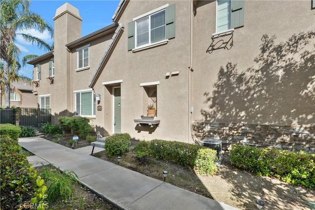 view of home's exterior featuring fence, a chimney, and stucco siding
