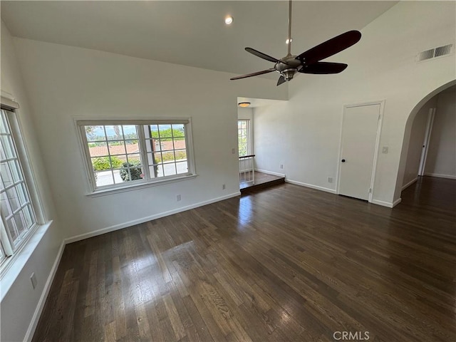 unfurnished living room featuring arched walkways, a ceiling fan, dark wood-style flooring, baseboards, and a towering ceiling