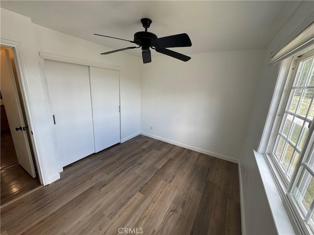 unfurnished bedroom featuring dark wood-style floors, a closet, baseboards, and ceiling fan