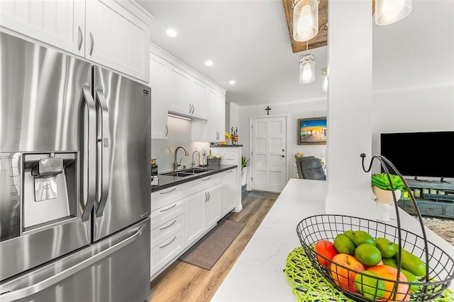 kitchen featuring stainless steel refrigerator with ice dispenser, a sink, wood finished floors, white cabinetry, and recessed lighting