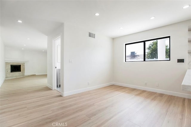 unfurnished room with a high end fireplace, light wood-style floors, recessed lighting, and baseboards