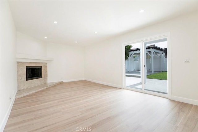 unfurnished living room with light wood-type flooring, recessed lighting, baseboards, and a premium fireplace
