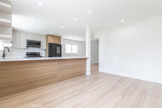 kitchen with stainless steel appliances, light countertops, light wood-style flooring, decorative backsplash, and recessed lighting
