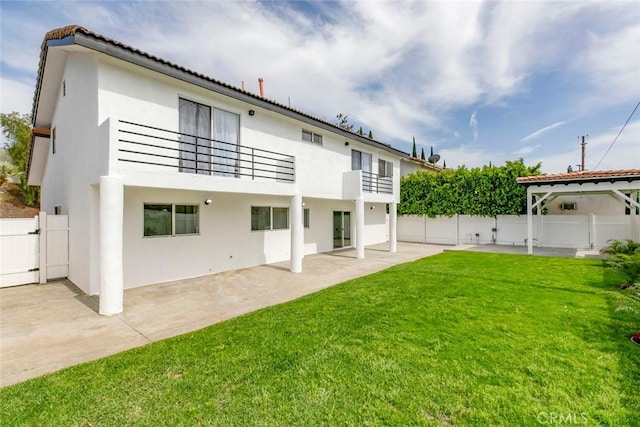 back of house featuring a balcony, a patio area, stucco siding, and a gate