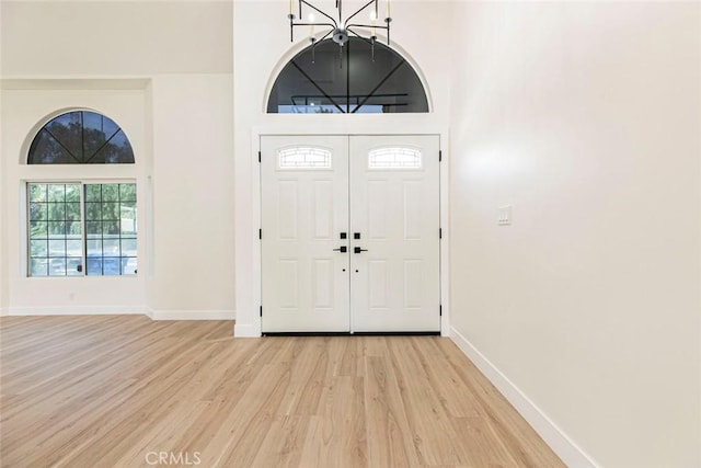 entrance foyer featuring light wood-type flooring, a chandelier, baseboards, and a high ceiling