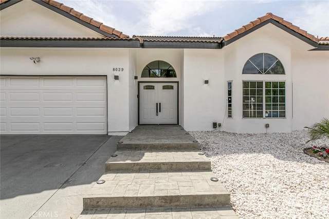 mediterranean / spanish house with stucco siding, a tiled roof, an attached garage, and concrete driveway
