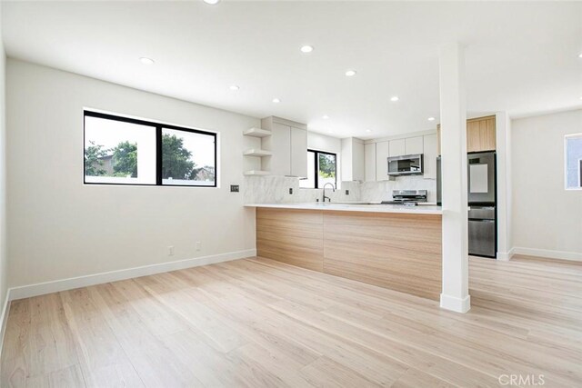 kitchen featuring stainless steel appliances, open shelves, decorative backsplash, light countertops, and light wood-style floors