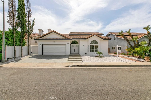 mediterranean / spanish-style home with stucco siding, a garage, fence, and driveway