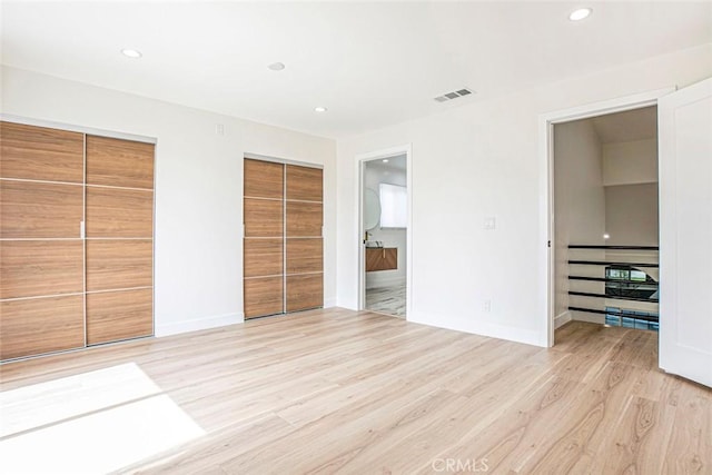 unfurnished bedroom with two closets, light wood-style floors, recessed lighting, baseboards, and connected bathroom
