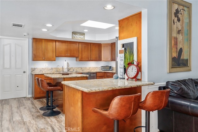 kitchen featuring a skylight, brown cabinets, light wood finished floors, stainless steel dishwasher, and recessed lighting