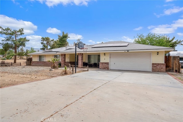 ranch-style home featuring brick siding, roof mounted solar panels, and a garage