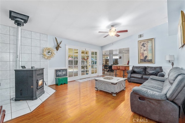 living room featuring a wood stove, a ceiling fan, light wood-type flooring, and lofted ceiling