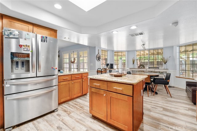 kitchen featuring stainless steel refrigerator with ice dispenser, light wood-type flooring, light stone counters, a center island, and plenty of natural light