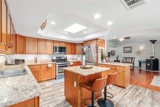 kitchen with appliances with stainless steel finishes, a sink, light wood-type flooring, a tray ceiling, and recessed lighting