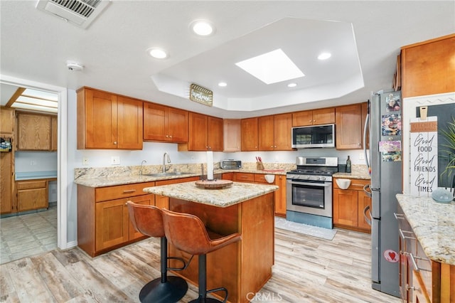 kitchen with stainless steel appliances, a raised ceiling, a sink, a skylight, and a kitchen island