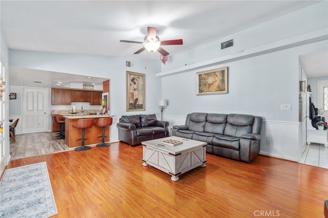 living room featuring a ceiling fan, light wood-style floors, and wainscoting