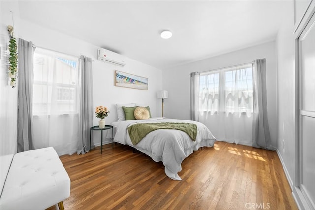 bedroom featuring an AC wall unit, multiple windows, wood finished floors, and baseboards