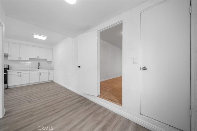 kitchen featuring white cabinets, light wood-style flooring, light countertops, stove, and a sink