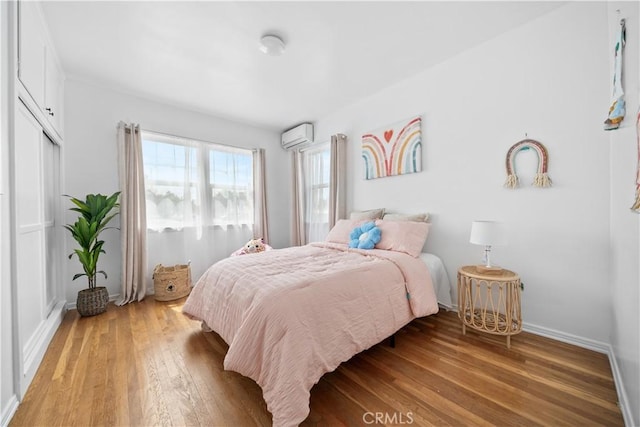 bedroom featuring a wall unit AC, light wood finished floors, and baseboards