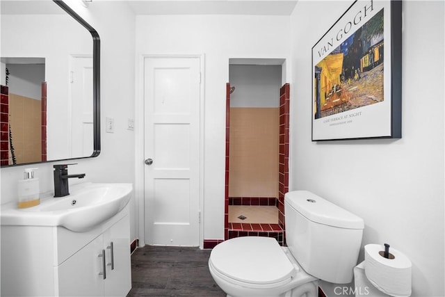 full bathroom featuring vanity, a tile shower, wood finished floors, and toilet