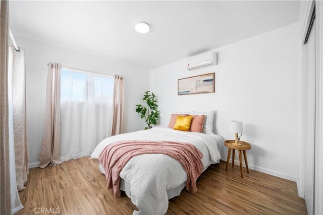 bedroom featuring a wall unit AC, wood finished floors, baseboards, and a closet