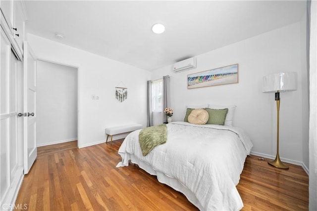 bedroom with an AC wall unit, wood finished floors, baseboards, and a closet