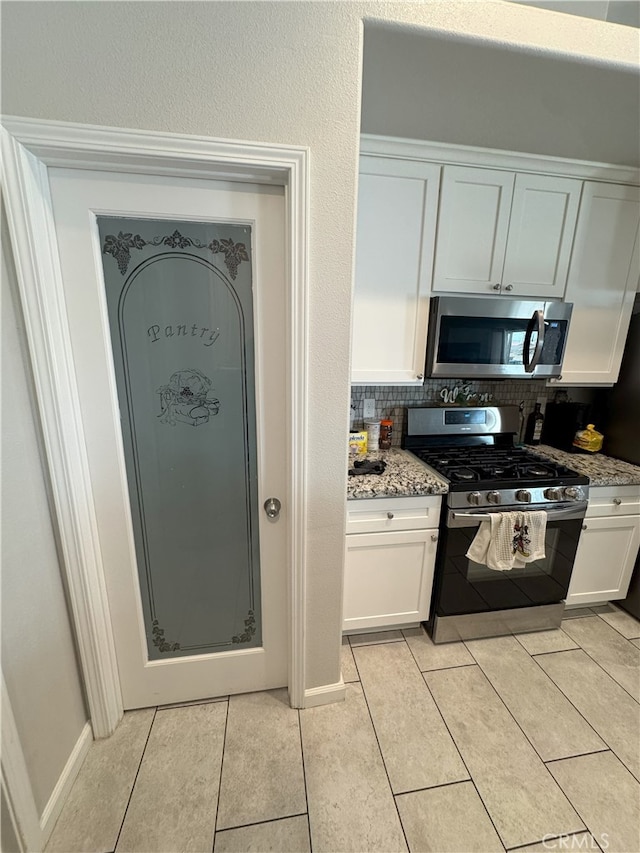 17602 Main St, Hesperia, CA 92345 - kitchen featuring stainless steel appliances, white cabinetry, tasteful backsplash, light tile patterned floors, and light stone counters