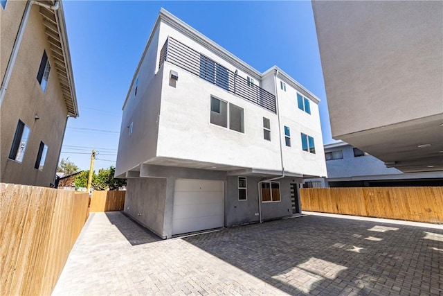 rear view of property with stucco siding, an attached garage, fence, and driveway