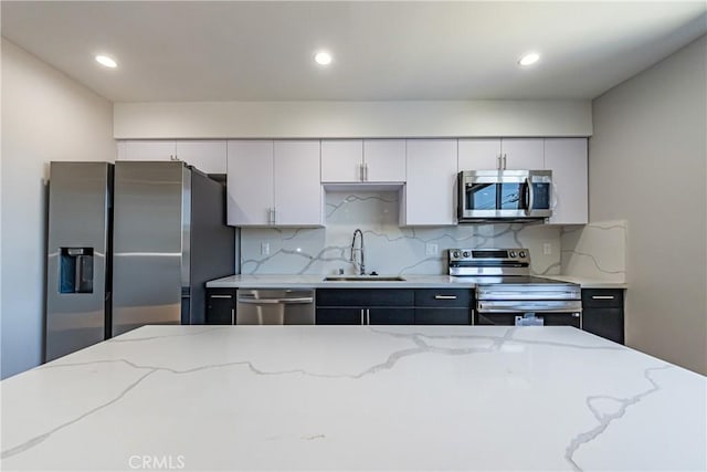 kitchen featuring appliances with stainless steel finishes, a sink, decorative backsplash, light stone countertops, and white cabinets