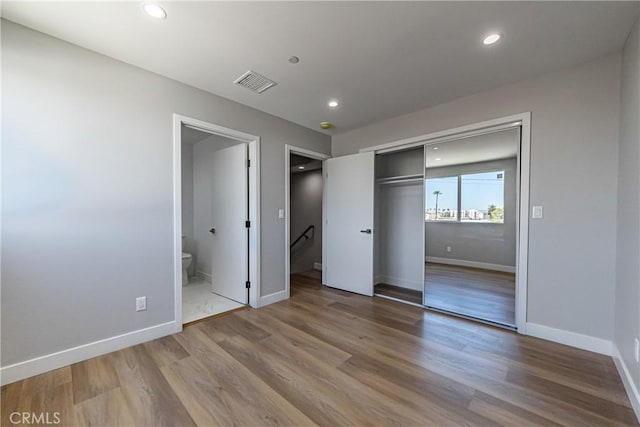 unfurnished bedroom featuring baseboards, wood finished floors, a closet, recessed lighting, and ensuite bath
