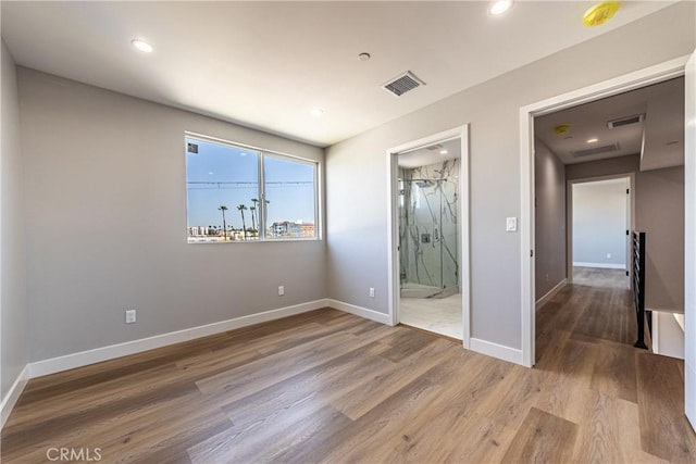 unfurnished bedroom featuring wood finished floors, baseboards, recessed lighting, and ensuite bathroom